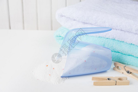 白色和蓝毛浴巾堆叠成白和蓝色毛浴巾从测量杯和木制衣板底白色面的木上洒落洗衣粉图片