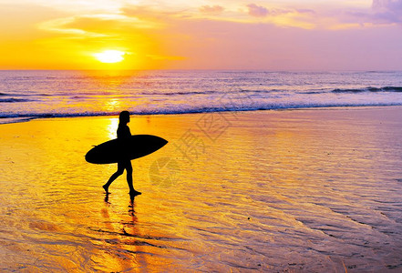 女人冲浪者在沙滩上行走日落时有冲浪板图片