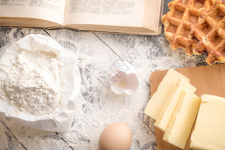 高角视图满桌面粉切片黄油蛋壳开放的古董烹饪书和新鲜的贝吉饼背景图片