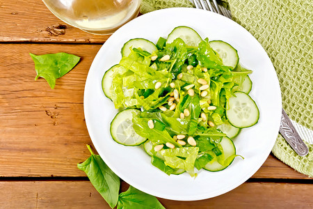 菠菜沙拉新鲜黄瓜Rukola沙拉雪松坚果和春洋葱盘上植物油餐巾和叉上木板底的头巾和叉子图片