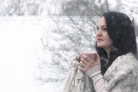 一个美丽的年轻黑发女人在下雪的时候喝热咖啡图片