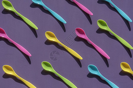 用一堆塑料小勺子以各种充满活力的颜色以对称排列紫色木制背景图片