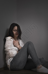 年轻女子情绪低落拉着衬衫遮盖自己坐在地板上靠墙图片