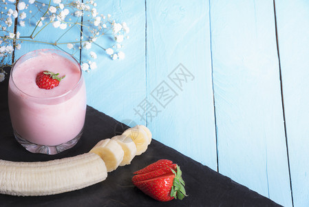 甜美的草莓和香蕉冰淇淋健康饮食概念用一杯新鲜的草莓和香蕉冰淇淋将水果切成黑色盘子蓝底阳光下图片