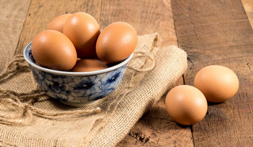 在木制板凳上以碗为新产有机鸡蛋在木制板凳上以碗为杯子安排褐色有机鸡蛋的东面背景将棕色有机鸡蛋安排在竹制木板桌上的布拉麻袋在木制板图片