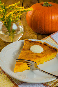南瓜馅饼加奶油叉子白餐巾玻璃花瓶和木本底黄色的米摩萨花图片