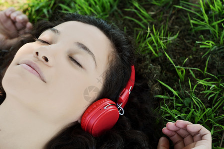 年轻拉丁女人的肖像带着耳机夏季在公园听音乐享受图片