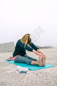 女青年在海岸边的瑜伽垫子上做腿部拉伸运动图片