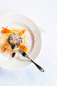 巧克力甜点巧克力味熔岩蛋糕香草酱柑橘白盘和叉子的金叶图片