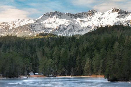 蓝冰湖环绕着长青的森林和雪地阿尔卑斯山脉在奥特里亚比伯维尔村附近阳光明媚的十二月一天背景图片