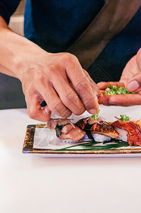 亚轮厨师在很多种日本寿司上放了切开的绿洋葱在陶瓷盘牛肉鹅肝上图片