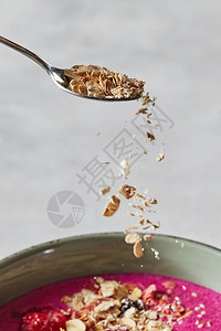 燕麦片从勺子上倒到盘碗里有新鲜果汁准备健康早餐燕麦片从勺子上倒到盘混凝土背景的梨子上在红沙倒图片