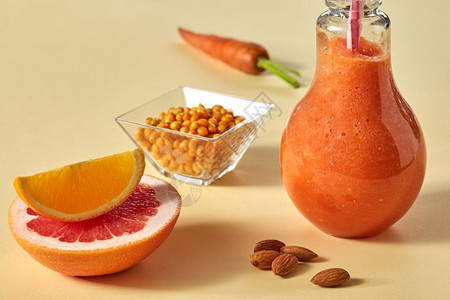 用胡萝卜葡萄果橙海角和杏仁在黄色纸底面的玻璃杯中饮用胡萝卜海角和杏仁在黄纸底面的玻璃杯中健康的脱毒冰图片