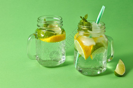 柠檬和冰水绿底玻璃中的塑料吸管柑橘水果片绿色底料上的夏季清新饮料玻璃罐中的自制火花鸡尾酒冷精或非夏季饮料的概念图片