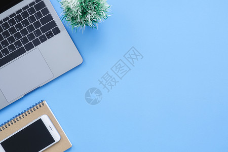 办公桌工作空间平面工作空间模拟照片用笔记本电脑智能手机和空白笔记本拍摄在蓝面背景上部蓝色背景工作桌概念图片
