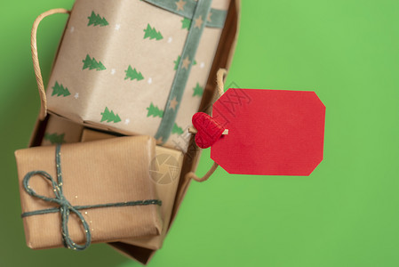 装满包礼物盒的纸袋上面有红色的空标签夹在手柄上绿色背景圣诞节框架上面有复制空间图片