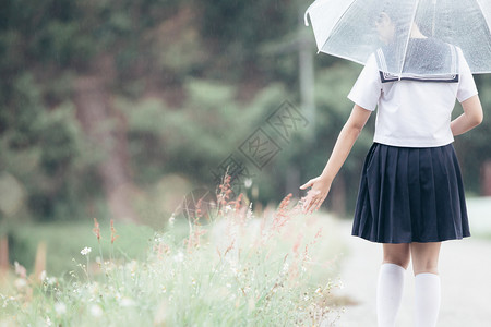下雨时在自然行走道上带着雨伞行走的亚裔女学生肖像图片