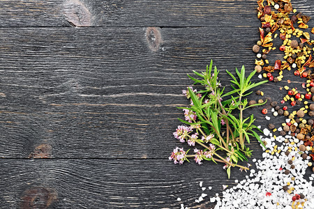 黑木板背景上含盐胡椒fenugrk种子的粉红色花朵图片