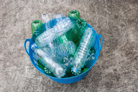 水泥地板上蓝色废物篮中的塑料瓶图片