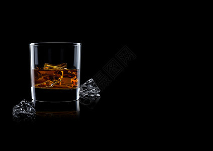 优雅的威士忌杯子冰块在黑色背景上反射图片