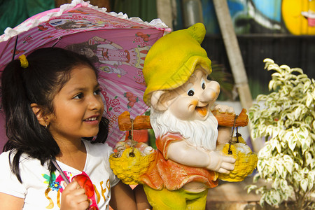 带着卡通像的印度小女孩笑着手持粉红色雨伞在花园里手持粉红色雨伞的印度小女孩笑着图片