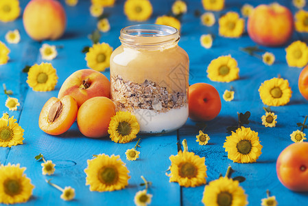 有桃酸和燕麦的罐子四周都是桃和黄色花朵放在蓝木桌上饮食早餐准备吃健康的食物图片