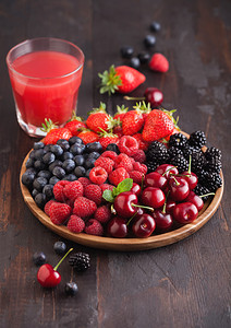 以圆木质盘装满果汁杯的圆木板在黑桌底的板上摆放草莓蓝黑和樱桃背景图片