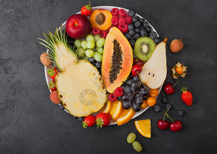 黑底的白盘中鲜生有机夏季浆果和异国水菠萝木瓜葡萄内啡橙杏仁基维梨淋巴樱桃和植物图片