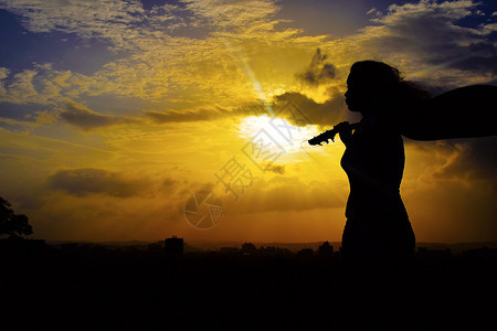 青年女孩怀抱着吉他在夕阳下沉思图片