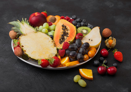 黑底的白盘中鲜生有机夏季浆果和异国水菠萝木瓜葡萄内啡橙杏仁基维梨淋巴樱桃和植物图片