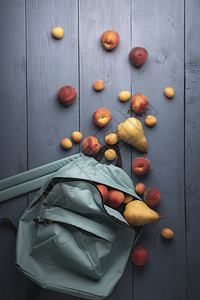 蓝底色背景上方的成熟水果桃子杏和蓝背包中的梨子背景图片