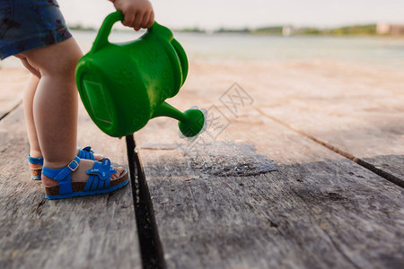 一个小女孩在玩木桥的水罐春天和夏园艺绿色水罐图片