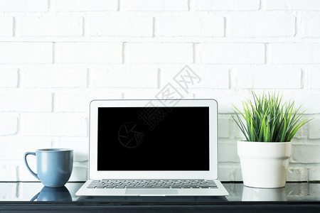 在屏幕上空着笔记本电脑咖啡杯和绿色植物锅放在桌上商业和技术工作空间概念图片