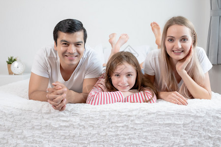 小女孩与父母一起在家中卧室的床上同父母一起微笑年轻幸福的家庭概念图片