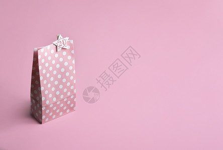 粉红色的纸袋上面有白点和24号放在粉红色背景上圣诞节的冒险日历概念圣诞节前夕的背景礼物主题图片