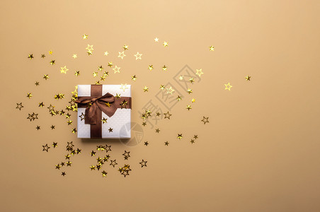 白色圣诞礼物盒有棕色的弓丝带和金面条星形在棕色背景上圣诞礼物概念节日礼物图片