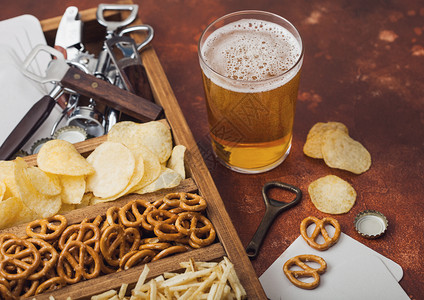 棕色厨房餐桌背景上装着一盒零食的杯式啤酒和开瓶器图片