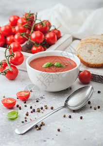 白碗盘的奶油番茄汤匙在浅底背景上一盒生西红柿和面包图片