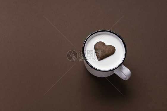 白杯牛奶上漂浮着棕色背景平板的热牛奶和巧克力饼干浪漫的饮料图片