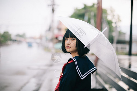 雨天时在乌拉班人行道上带着雨伞走的亚裔女学生肖像图片