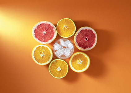 夏季鸡尾酒成分含柑橘水果和玻璃在阳光下橙色底面有冰块新鲜橙子和葡萄果切成两半背景图片