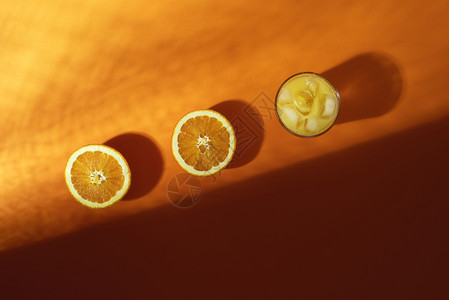 鲜橙汁在玻璃中冰块和橙子果汁在冰冷的熔岩背景阳光和阴影下被切成一半寒冷的夏季饮料图片