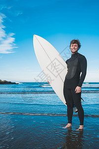 年青的冲浪者站在海洋中穿着黑色冲浪西装的板运动和水上的概念图片