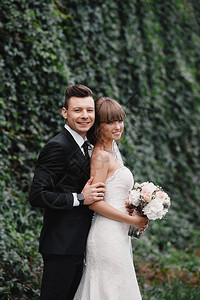 新婚夫妇郎和婚夫妇站着并拿花束盛放粉色和紫的花绿园里有色的带丝关于自然的婚礼仪式图片