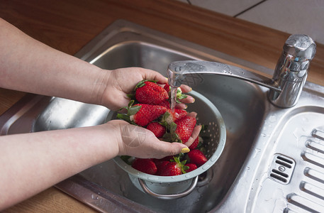 在厨房水槽里洗熟草莓的妇女在自来水管下图片