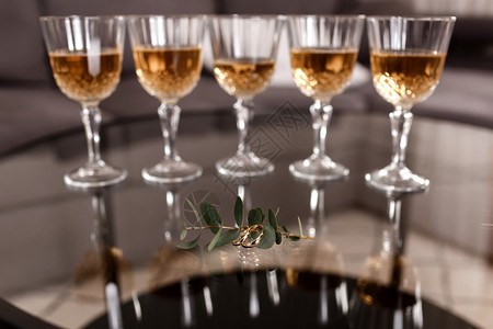 金色结婚戒指放在一张玻璃桌子上面有叶卡利普图斯香槟杯放在背景上有选择的焦点图片