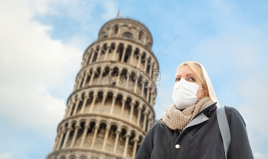 身戴面罩的年轻女子在意大利的比萨斜塔附近走过图片