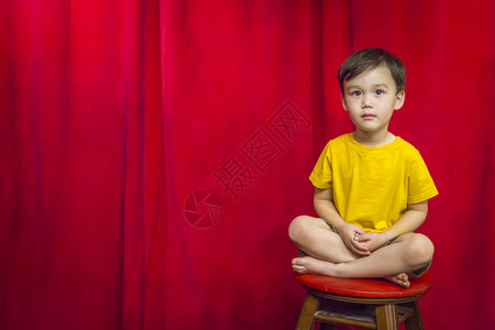 英俊的混血男孩坐在凳子上站红幕前图片
