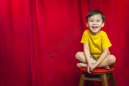 坐在凳子上红幕前的混血男孩图片