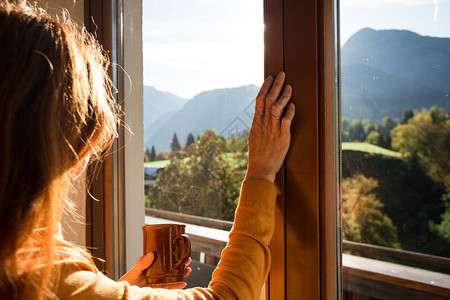 女孩拿着一杯咖啡看窗外的山上背景图片